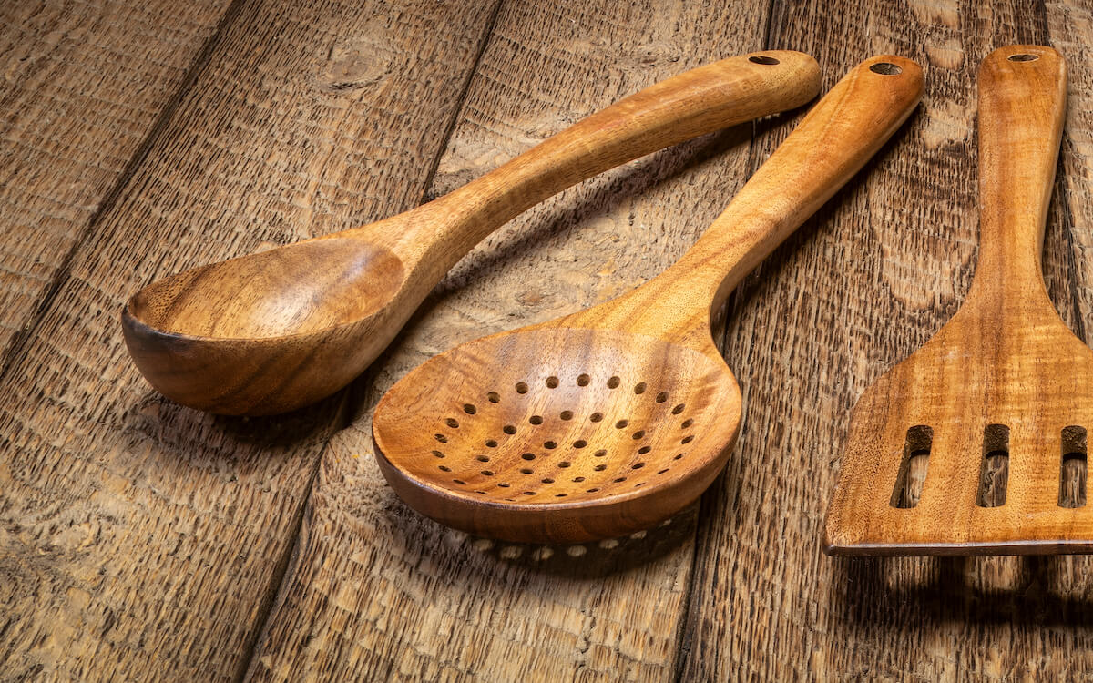 Wooden salad spoon, wooden strainer spoon, and wooden spatula resting on a table