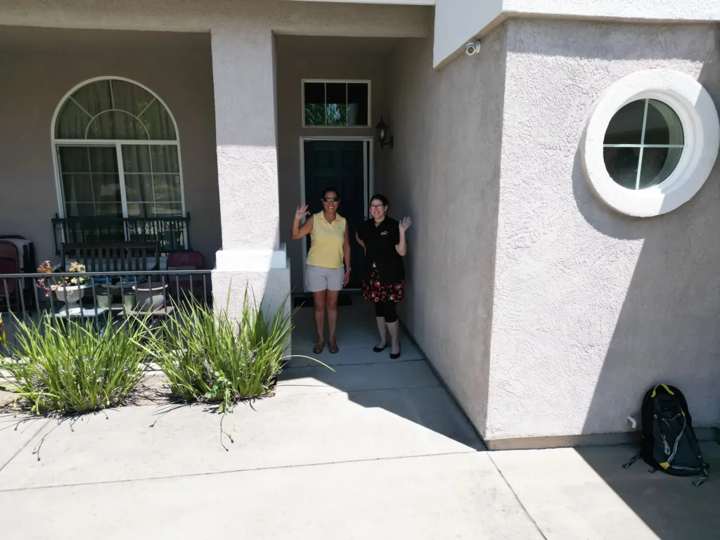 Mayor of West Sacramento and an ACR Solar representative standing on the front porch, smiling and waving, with newly installed solar panels on the roof.